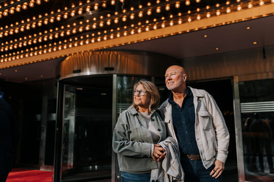 Smiling male and female senior friends standing outside movie theater