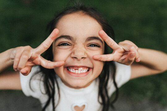 Portrait of happy elementary girl showing peace sign at park