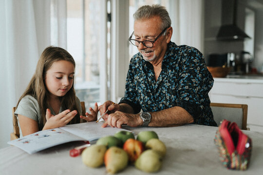 Senior man helping granddaughter with homework at home