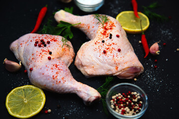 Raw chicken legs and spices on a black background.