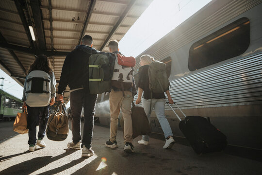 Rear view of family with backpacks and luggage walking near train at railroad station