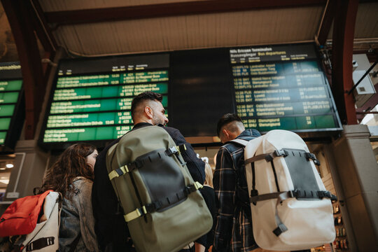 Rear view of family with backpacks standing against arrival departure board at railroad station