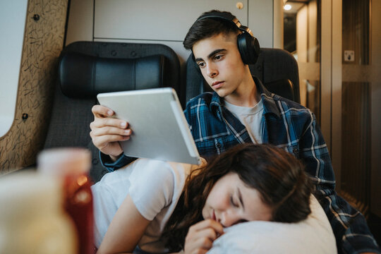 Boy watching tablet PC with sister sleeping on lap in train