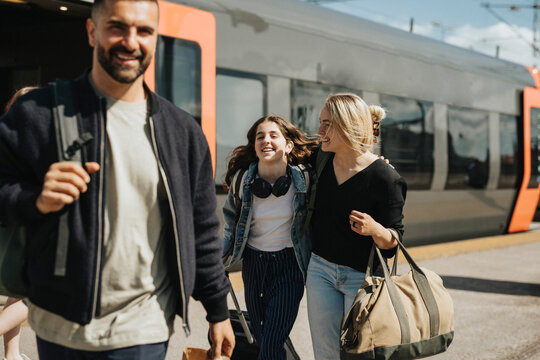 Happy family disembarking from train at station during sunny day