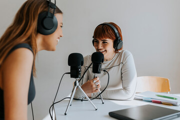 Happy teenage girls talking during podcast at desk in classroom