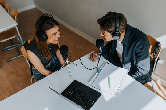 Smiling male and female students looking at each other during podcasting in classroom