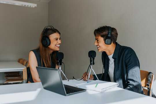 Happy male and female students looking at each other during podcasting in classroom - Powered by Adobe