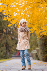 Caucasian girl in a beige coat and beret walks in the park in autumn.