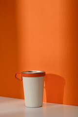 A white travel cup with handle over orange wall. Tumbler beverage container and Eco friendly...