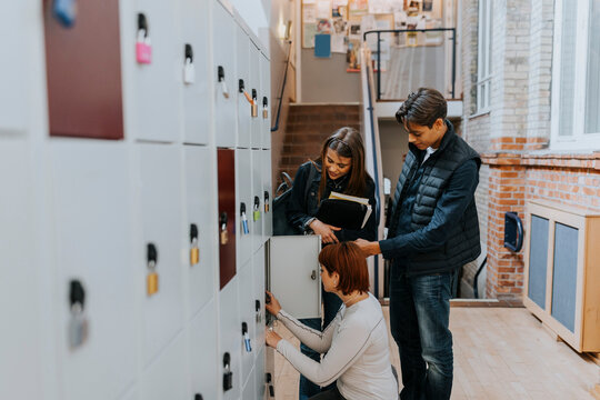 Multiracial friends standing by female student by locker in corridor