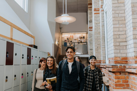 Happy male and female students walking by locker in school corridor