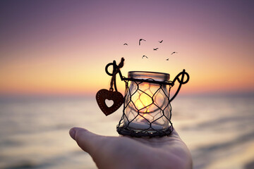 schöne Laterne mit Herz am Strand im Sonnenaufgang in der Hand halten