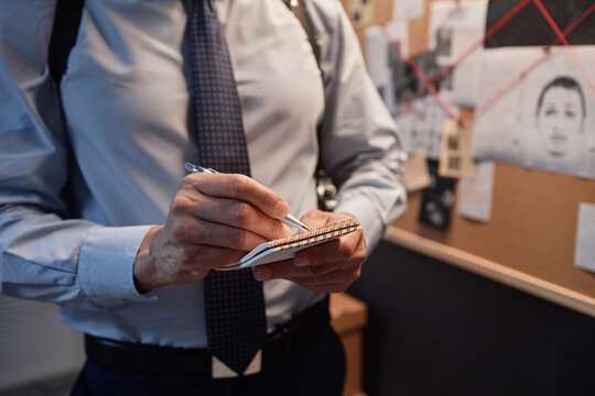 Close up of male detective taking notes while standing by evidence board and investigating crime case, copy space