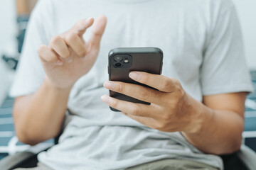 Hands of Asian man holding checking touching scrolling smartphone from bed room