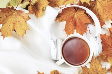 A Cup of hot coffee or tea with autumn leaves and headphones on a knitted white plaid background