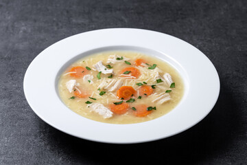 Chicken soup with vegetables on black slate background