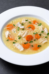 Chicken soup with vegetables on black slate background. Close up