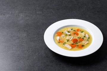 Chicken soup with vegetables on black slate background. Copy space