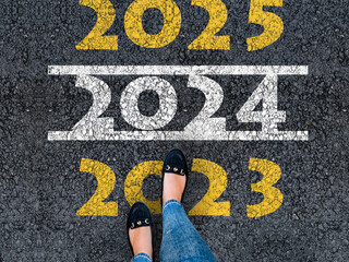 happy new year 2023. lets start 2023. woman legs in shoes walks on asphalt road next to number 2024 and 2025 She is standing on number 2023.
