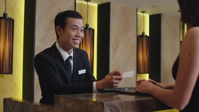 Medium shot of female tourist taking key cards from rooms while checking in, standing at hotel reception and talking to manager