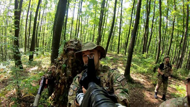 POV Close-up group of soldiers aiming with gun while moving through forest during military action. Squad of equipped fighters in camouflage uniform in forest. 