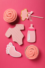 Cupcakes and paper baby things on pink background, top view