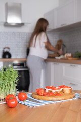 Pregnant young woman preparing healthy sandwiches with microgreens and vegetables at home in the kitchen