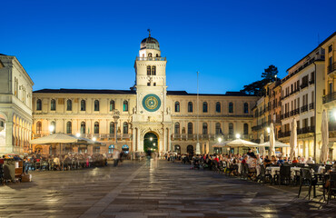 Fototapeta na wymiar Padua, Italy - October 1, 2023: Piazza dei Signori or Piazza della Signoria in the evening. The square is dominated by the famous Clock Tower. People sitting at the tables in the bar or walking around