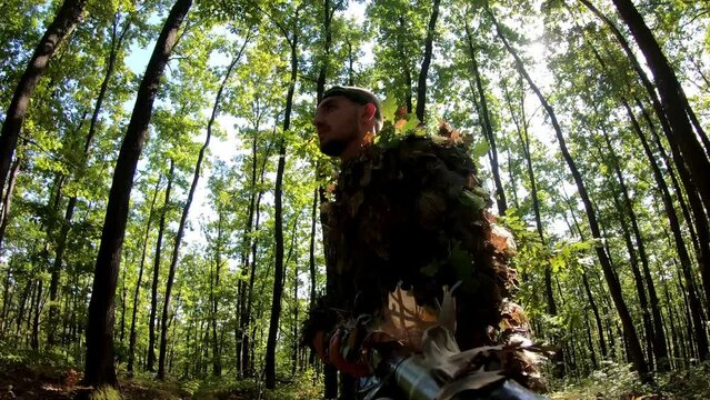 Man in Authentic Camouflage Suit with a Sniper Rifle Gun and Playing an Airsoft Game on a Real Warfare Field with Tries and Wooden Shelters in a Forest.