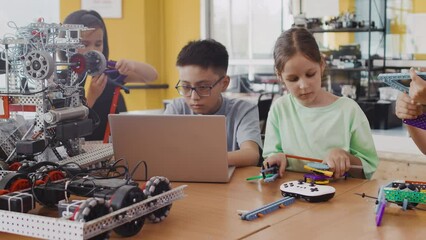 International group of a children in a class at a robotics lesson sitting at the table and assembling modules for moving robot in collaboration with each other. Concept of technological education