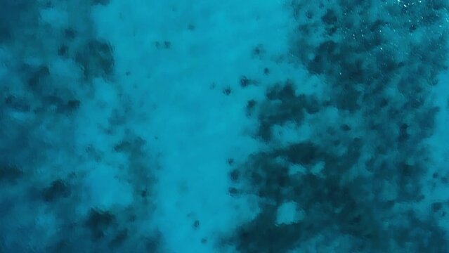Clear turquoise textured water with sandy bottom and rocky benthos, drone top down