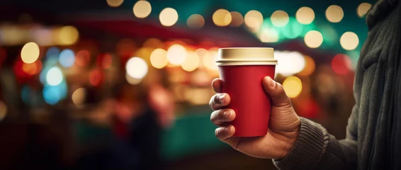 Kussenhoes Hand with cup of hot drink at Christmas fair. Enjoying Christmas Market, blurred people in the streets and near stalls with bokeh light background. street evening city lights.  © Chrixxi