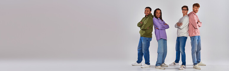 multicultural men standing back to back and smiling at camera on grey backdrop, diversity, banner
