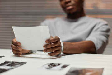 Close up of African American man wearing handcuffs looking at pictures in police department, copy space