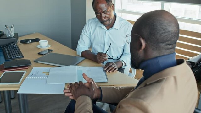 High angle tilt slowmo shot of black male employee in wheelchair talking to black male boss about business documents in directors office
