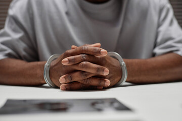 Close up of anonymous black man wearing handcuffs sitting at table in police department with hands...