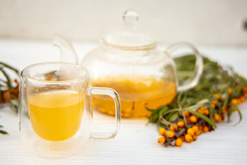clear glass cup filled with aromatic sea buckthorn tea, alongside a transparent teapot