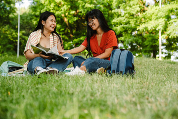 Two asian female students doing homework together while sitting on grass in park