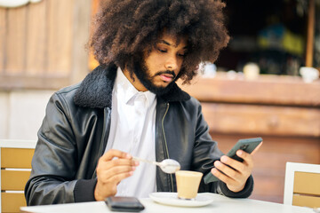 an african-american man looking at his cell phone while drinking coffee