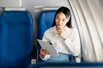 Young Asian executive excels in first class, multitasking with digital tablet, laptop and...