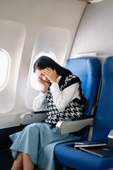 Photo of a frustrated woman sitting on an airplane with her head in her hands. Asian woman sitting...
