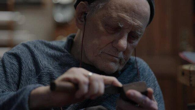 Senior gray haired male master in a wheelchair working at his workshop sharpening japanese deba knife