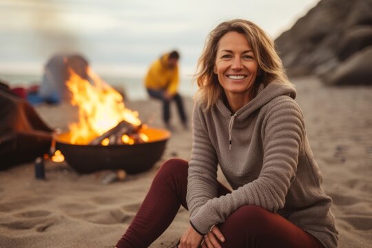 Portrait of smiling woman sitting by bonfire on beach in autumn