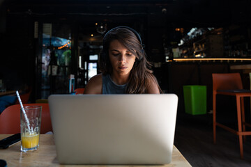 Young hardworking freelancer business woman or college student work and study online on laptop computer while sitting in cafeteria or coffee shop typing and drinking orange juice