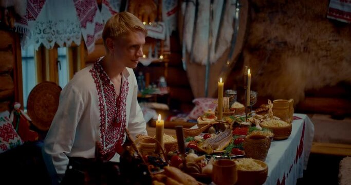 history of ancient Slavic village, blonde man meeting guests in hut with served table, 4K, Prores