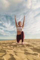 Sun Salutation Yoga on Beach - Vertical capture of a front-facing young woman in her twenties...