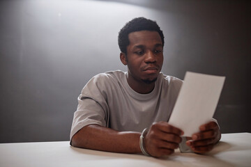 Portrait of Black young man looking at picture of evidence in police station