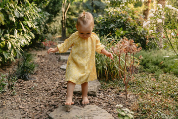 Cute little girl in stylish yellow dress walk in backyard garden.