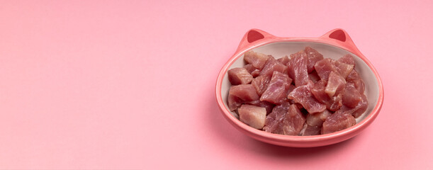 Organic raw meat pieces in a pink bowl with tears on a pink background with copy space. Food for animal. Banner