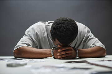 Portrait of Black man as criminal in handcuffs laying head on table in desperation, copy space